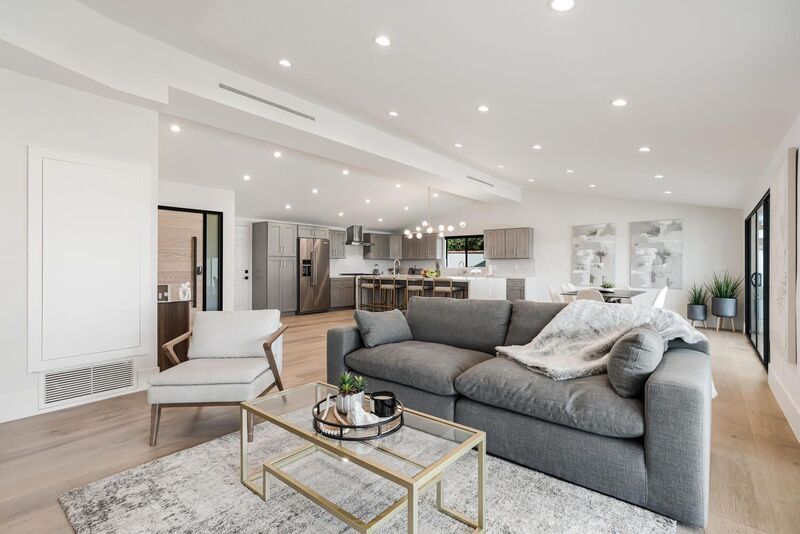 Modern living room with gray sofa, kitchen in the background, and hardwood floors.