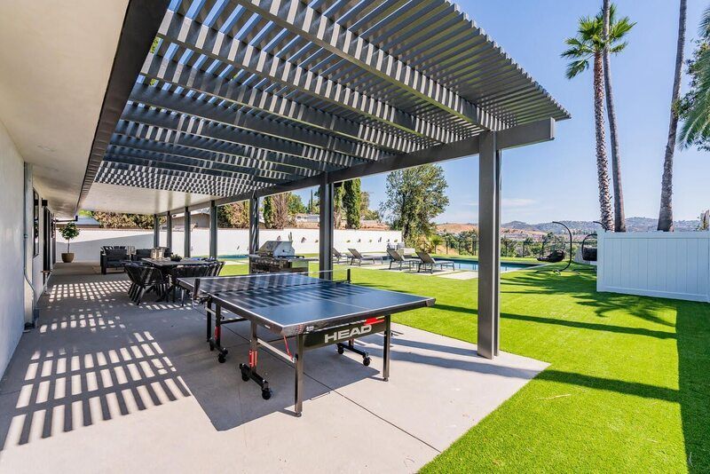 Patio with table tennis, dining set, and pool; sunny day, pergola shade.