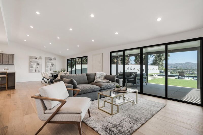 Spacious living room with gray sofa, sliding doors to backyard view, wood floors, modern furniture.