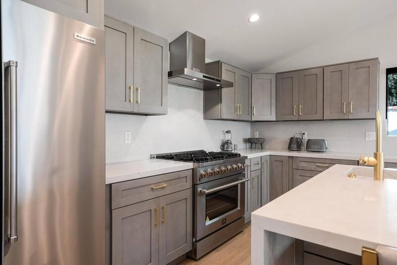 Gray and white modern kitchen with stainless steel appliances and gold hardware.