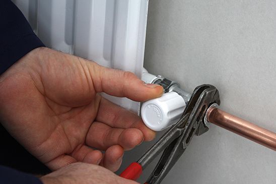 A person is fixing a radiator with a pair of pliers.