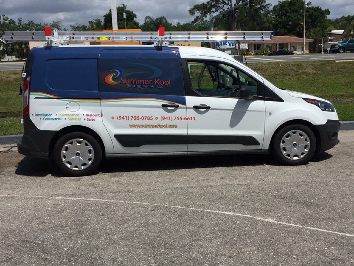 White and blue company van parked outside, with ladder on top