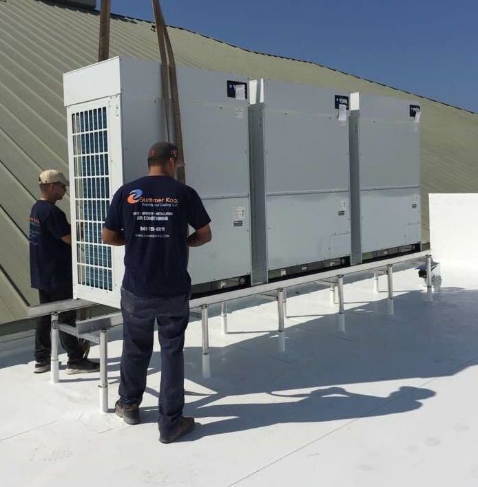 Two men on a rooftop installing HVAC units