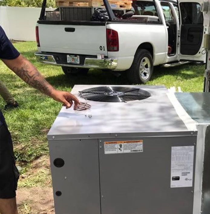 Man points to an air conditioner unit. A white truck is in the background