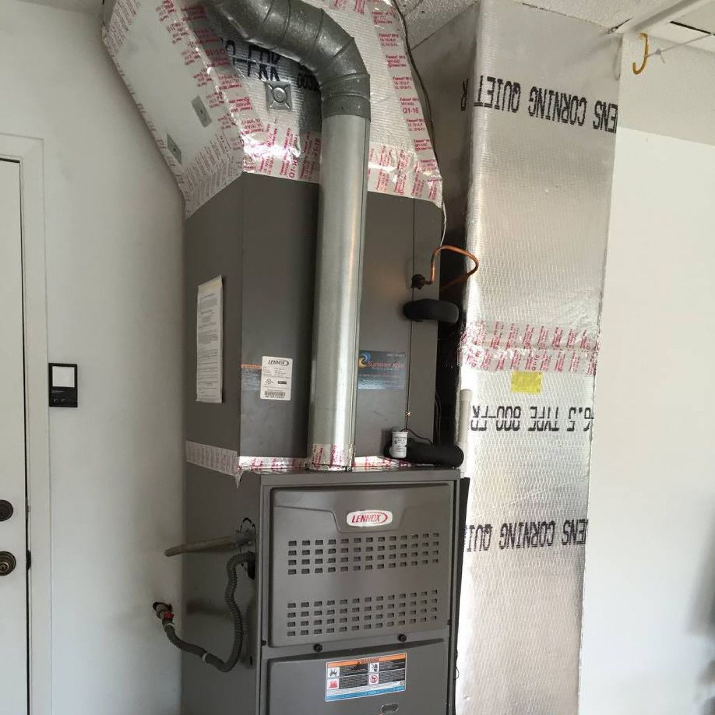 A Lennox furnace in a white room, with ductwork wrapped in reflective insulation