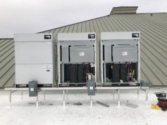 Three rooftop electrical units, one closed and two open, on a gray roof