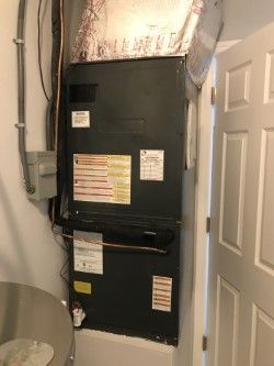 Furnace in a utility closet next to a door. Gray metal unit with ductwork, pipes, and labels