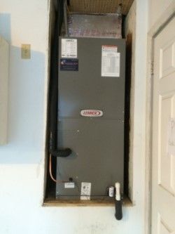 A gray Lennox HVAC unit installed in a wall cavity next to a white door