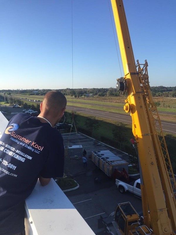 Man watches a crane lift something on a rooftop