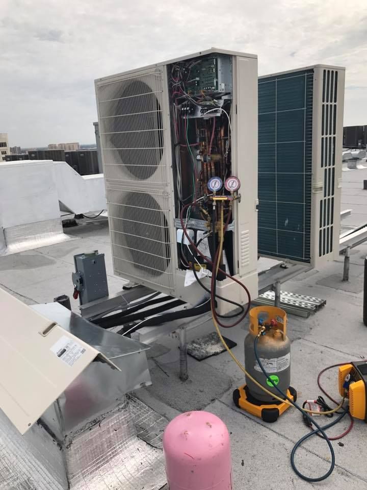 HVAC units on a rooftop. Open unit with gauges attached, yellow refrigerant tank, tools, overcast day