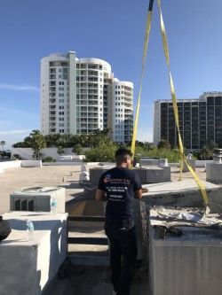 Man in blue shirt on rooftop, lifting equipment with yellow straps 