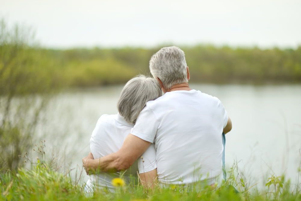 An Elderly Couple is Sitting in the Grass Near a Lake — Bull Family Funerals in Warialda, NSW