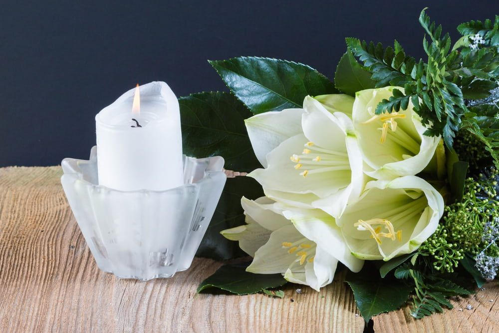 A Candle is Sitting Next to a Bouquet of White Flowers on a Wooden Table — Bull Family Funerals in Warialda, NSW