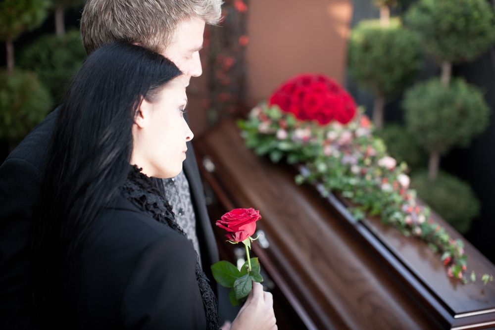 A Man and a Woman Are Standing Next to a Coffin at a Funeral — Bull Family Funerals in Moree, NSW