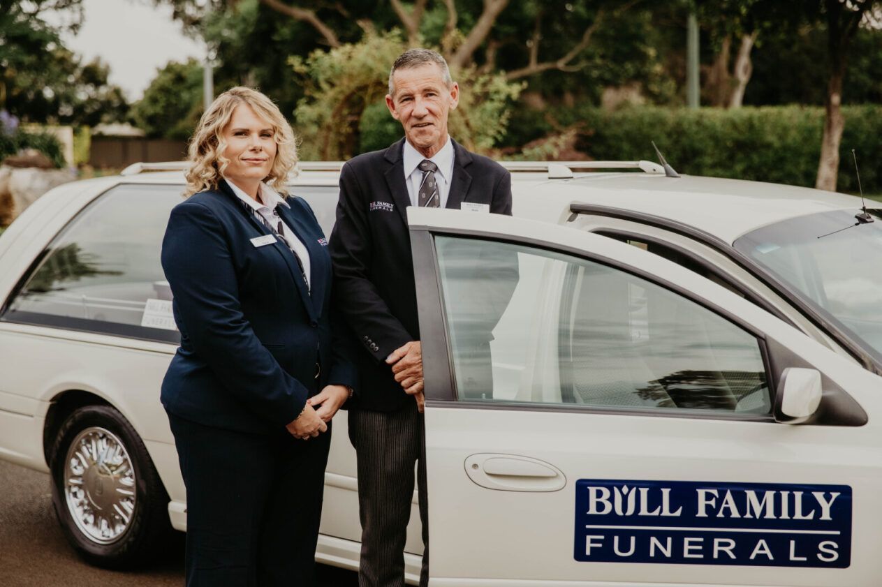 A Statue of an Angel Sleeping Next to Flowers on a Wooden Table — Bull Family Funerals in Inglewood, QLD