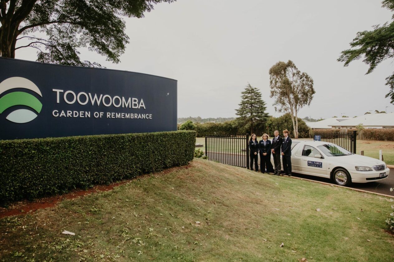 A Group of Men Are Carrying a Wooden Coffin With Flowers on It — Bull Family Funerals in Inglewood, QLD