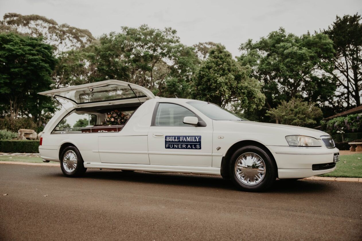 A White Coffin Decorated With Red and Green Flowers and a Candle — Bull Family Funerals in Goondiwindi, QLD