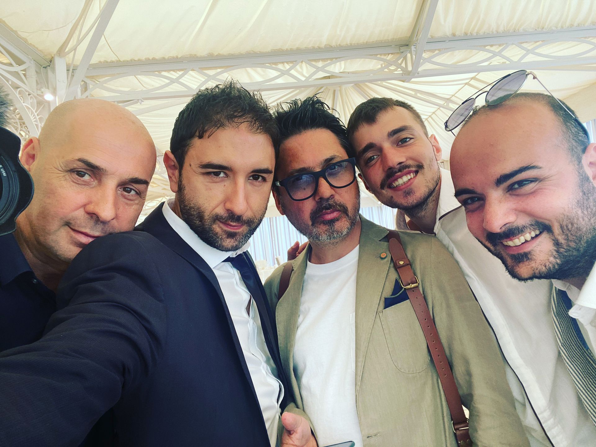 Cinque persone in posa ravvicinata in un ambiente interno, sotto un baldacchino bianco, sorridono all'obiettivo.