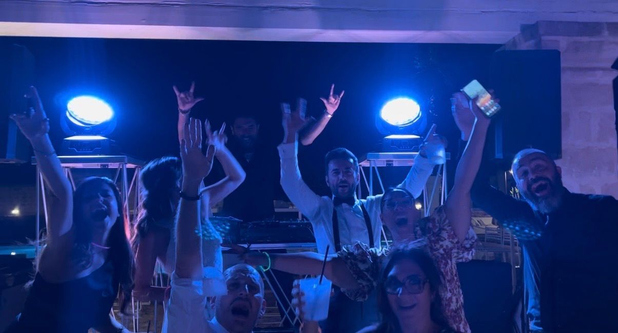 DJ mixa musica in una festa vivace, con gli ospiti che ballano sotto calde luci a catena e colorate luci di scena.