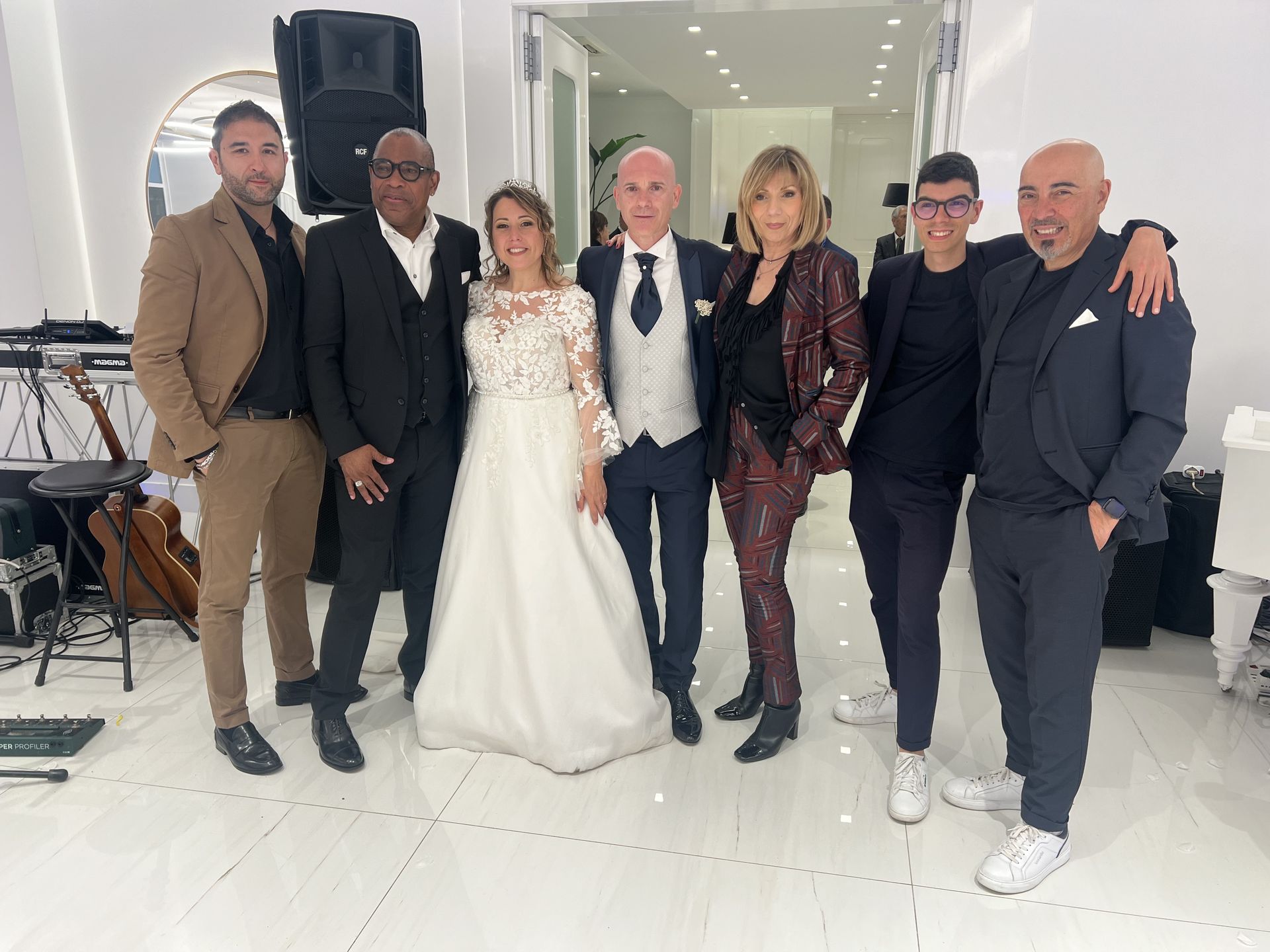 Sei persone in posa insieme durante un evento formale al chiuso, indossando abiti eleganti e completi da sera.