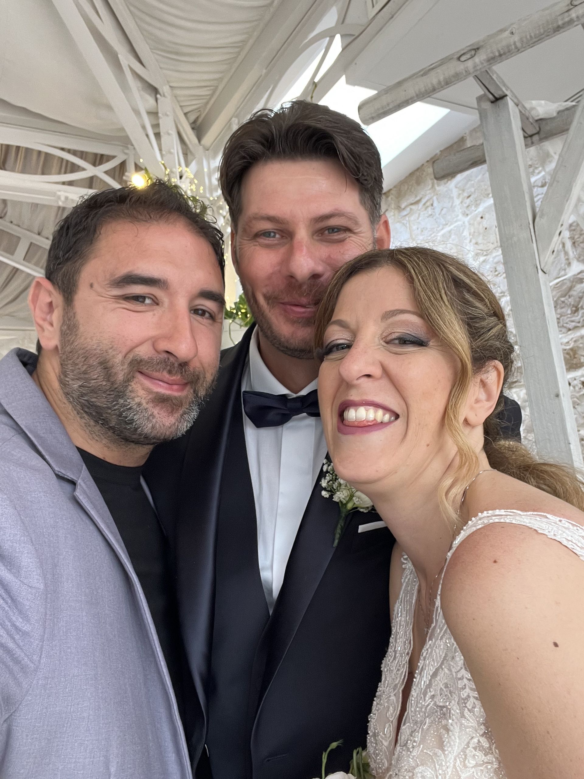 Tre persone sorridenti si scattano un selfie durante un evento all'aperto, con travi bianche sullo sfondo.