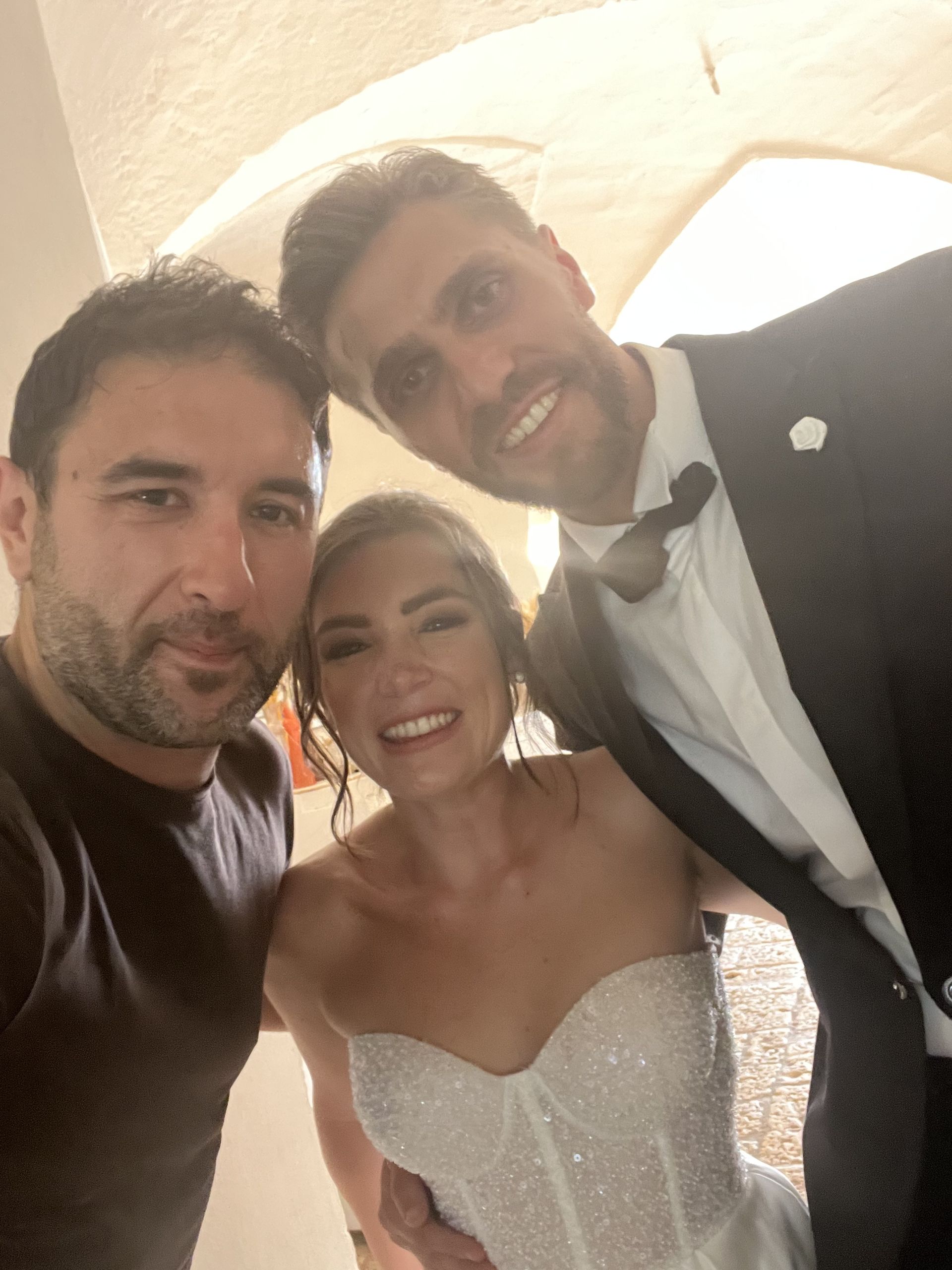 Tre persone sorridenti in posa in interni, una con un abito bianco e l'altra con uno smoking.