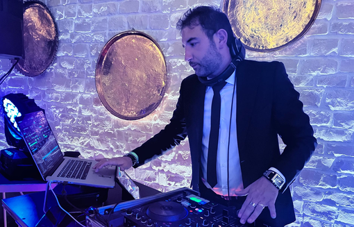 Un DJ regola i controlli di un mixer e di un giradischi in uno studio illuminato da una luce calda.