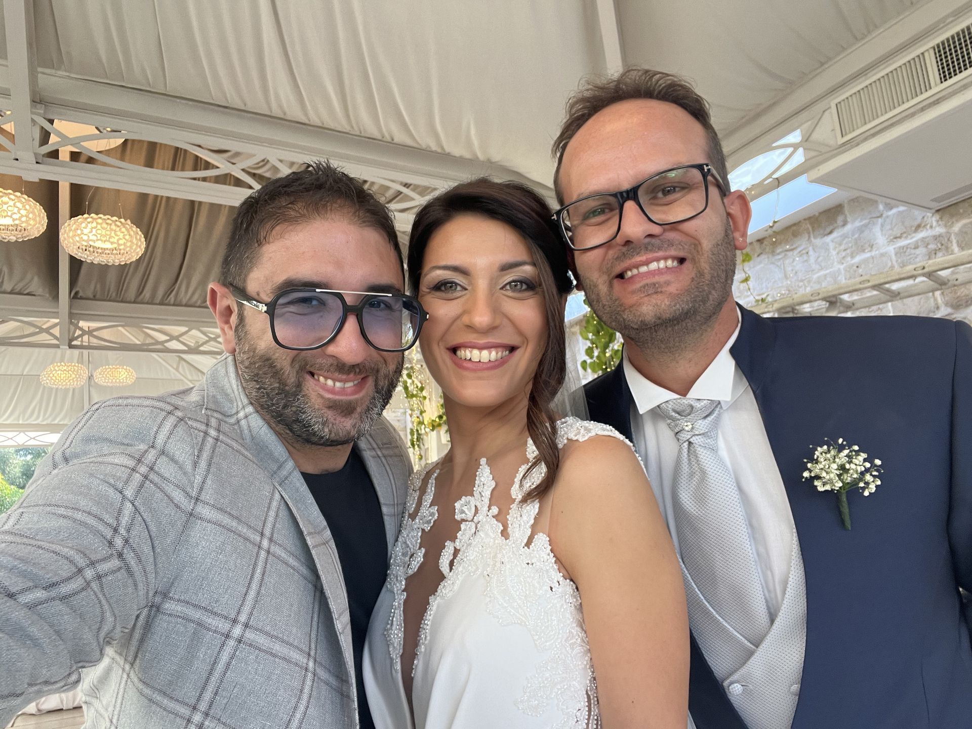 Tre persone sorridenti in abiti formali a un matrimonio sotto un tendone
