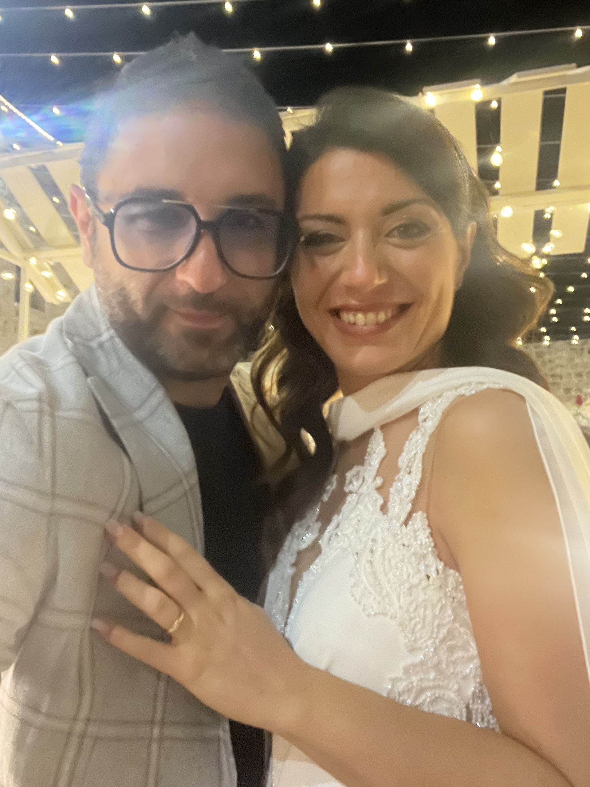 Una coppia sorridente posa insieme durante una festa serale, con delle luci decorative sullo sfondo.