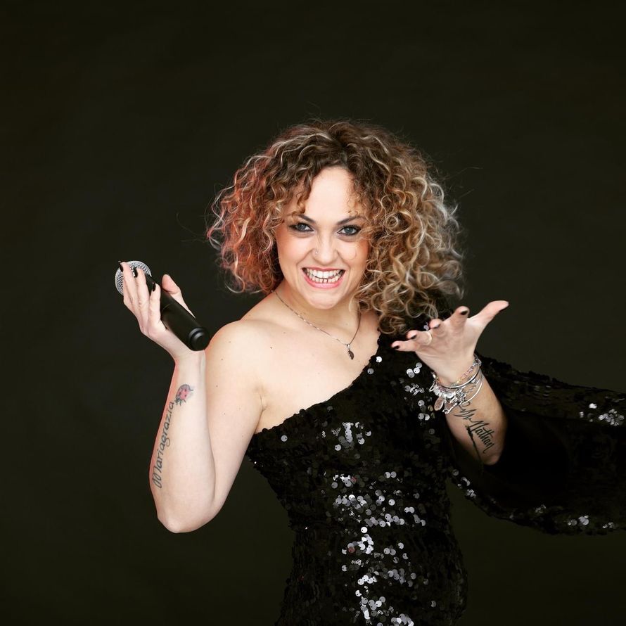 Donna sorridente con un abito nero tempestato di paillettes in posa su uno sfondo scuro