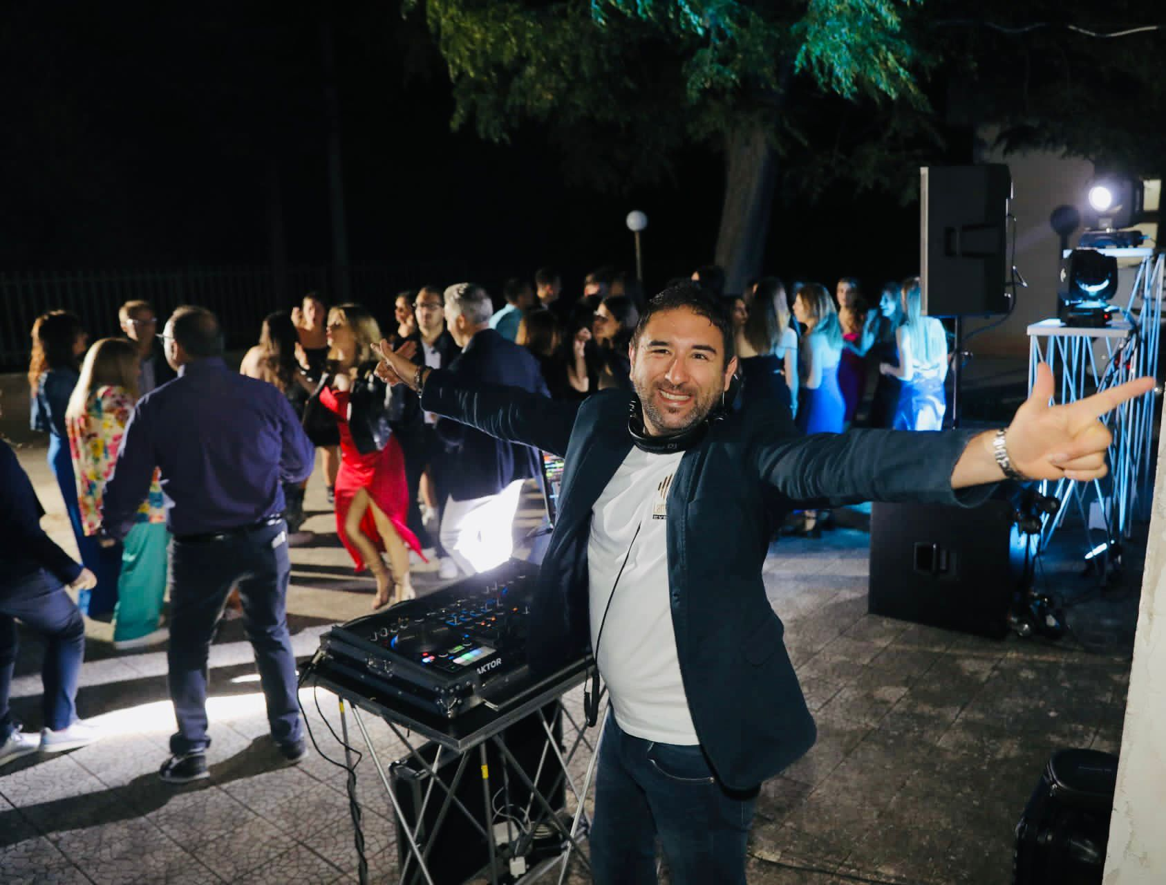 Festa notturna all'aperto con un DJ davanti agli ospiti che ballano, con il braccio alzato accanto all'attrezzatura audio.