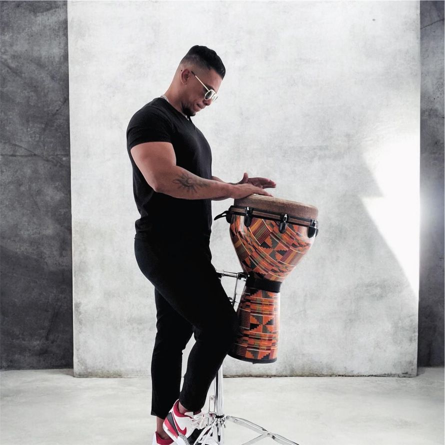 Un uomo in piedi suona un djembe decorato in uno studio dall'atmosfera minimalista.