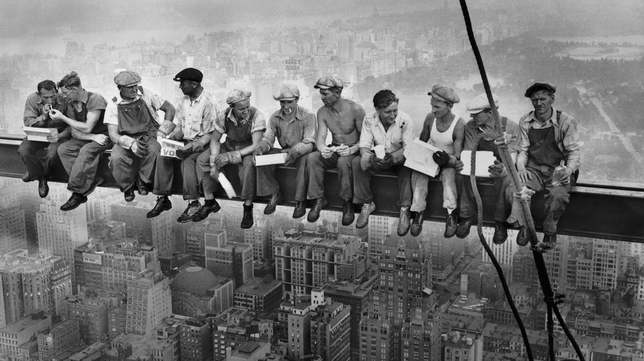 A group of men are sitting on a ledge overlooking a city.