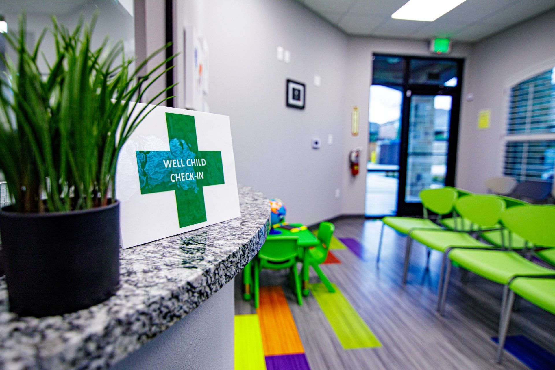 A waiting room with green chairs and a green cross on the counter.