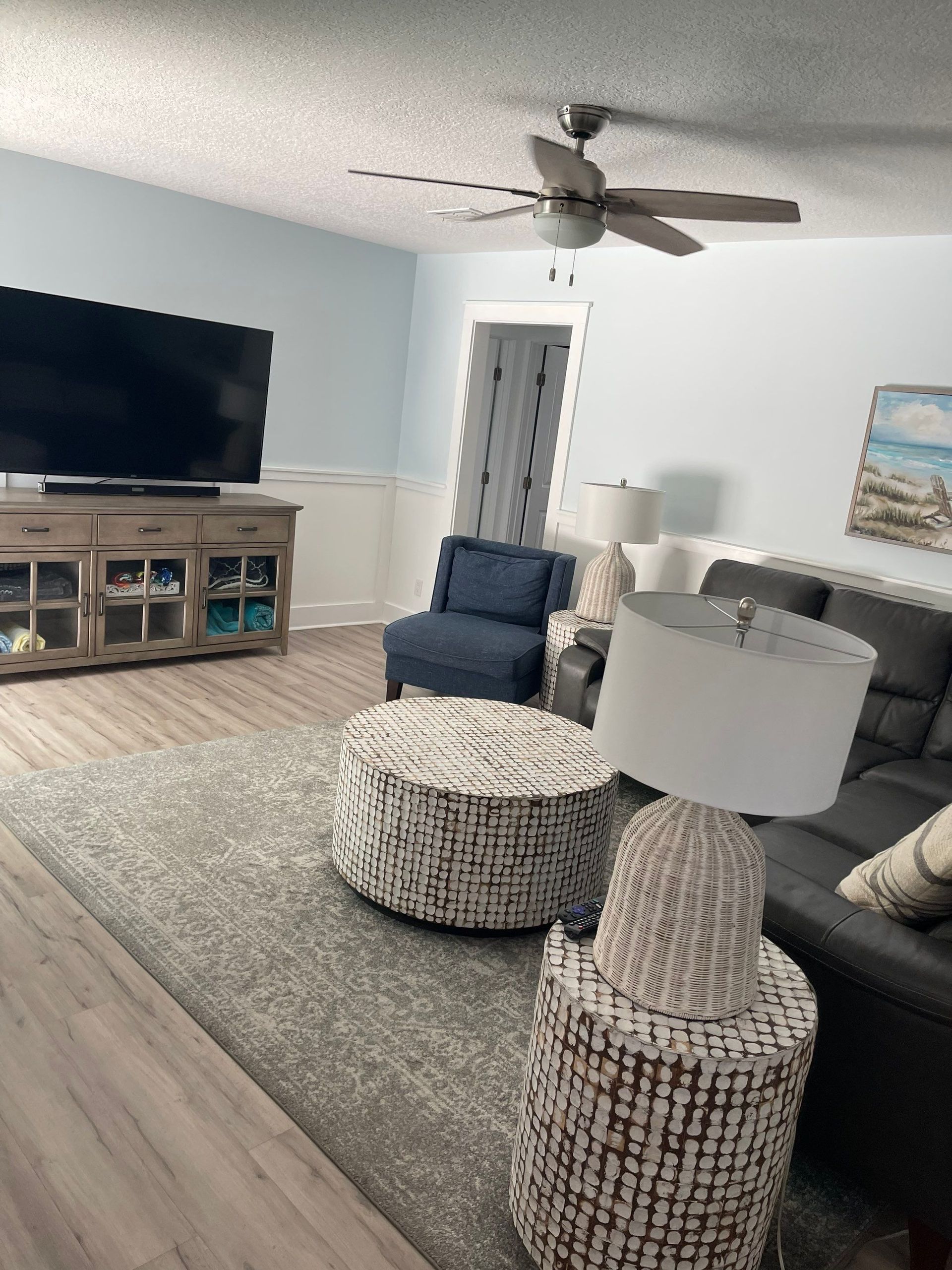 A living room with a couch , chair , ottoman , lamps and a flat screen tv.