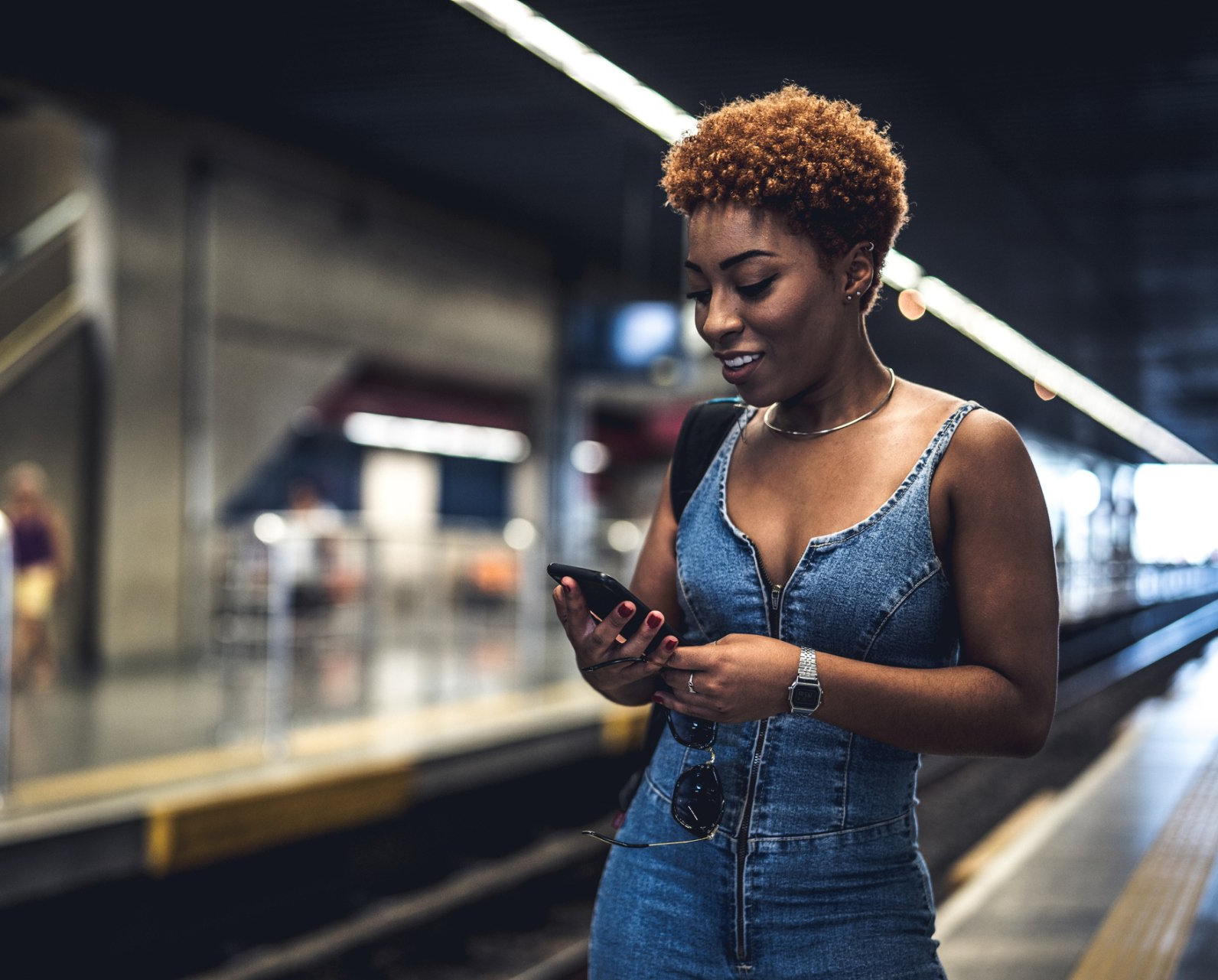 Mulher conhecendo os compromissos da XP Educação no celular enquanto espera pelo metrô