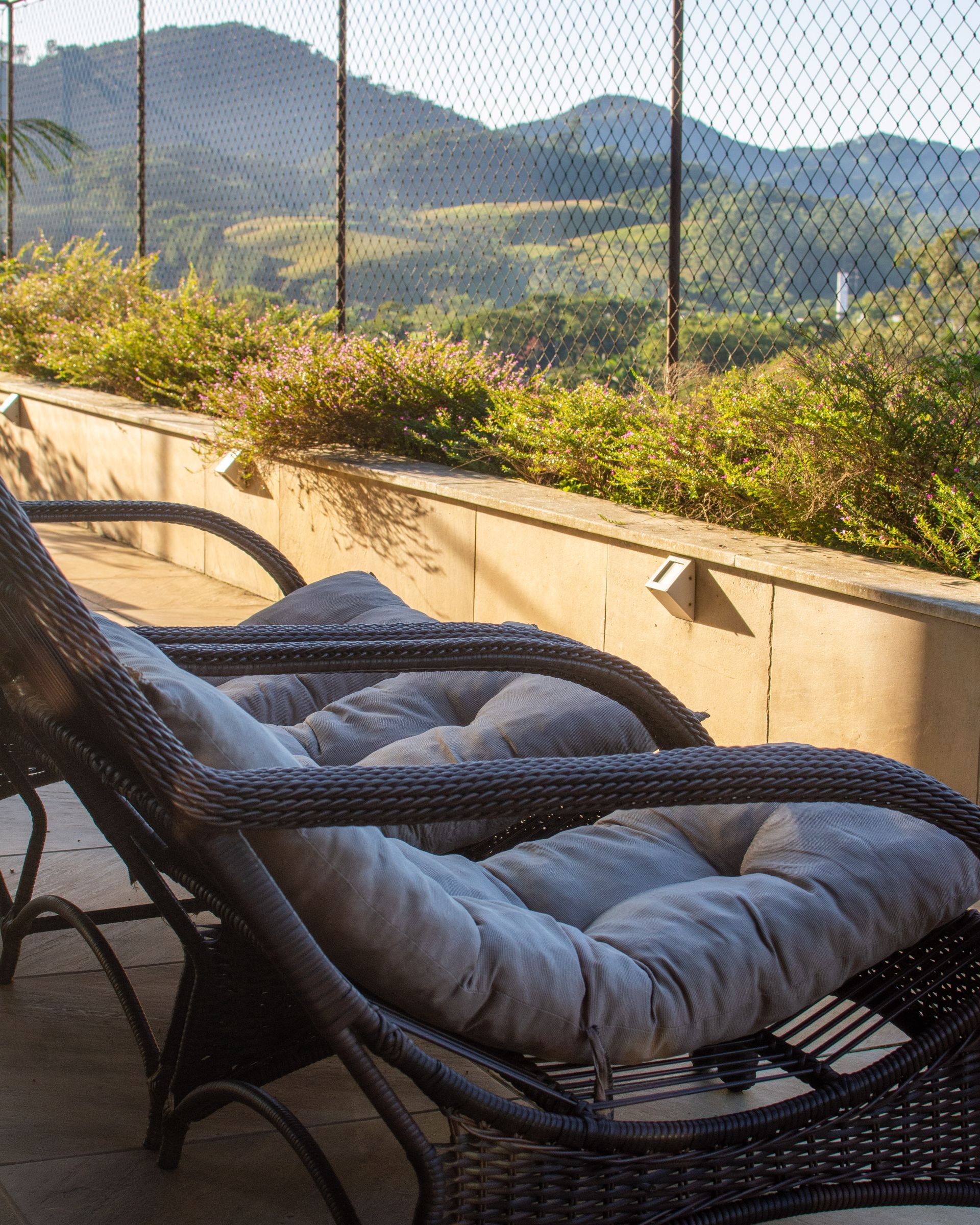 A wicker chair with a grey cushion is sitting on a patio with mountains in the background.