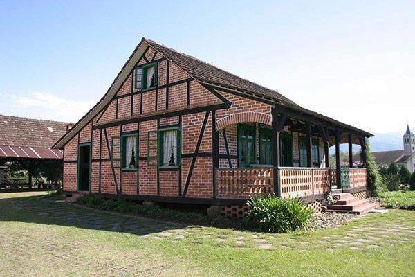 A large brick house with a wooden roof is sitting on top of a lush green field.