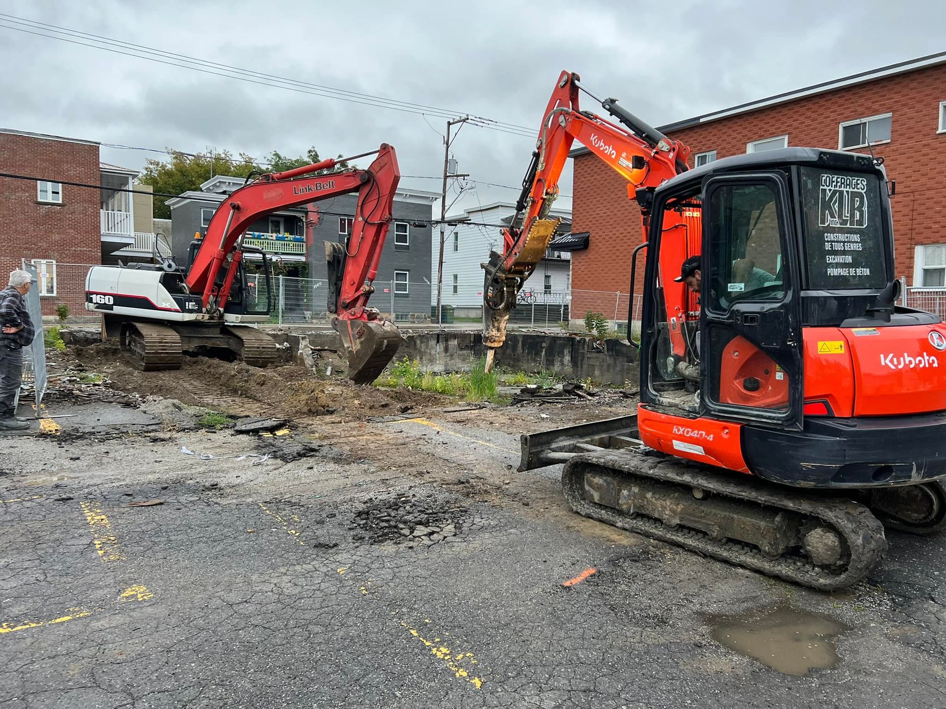Deux excavatrices travaillent sur un chantier devant un bâtiment en briques.