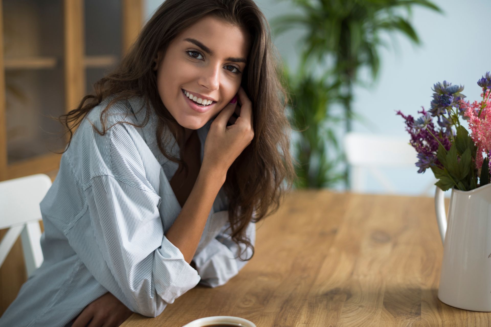 A woman is sitting at a table with a cup of coffee and flowers.