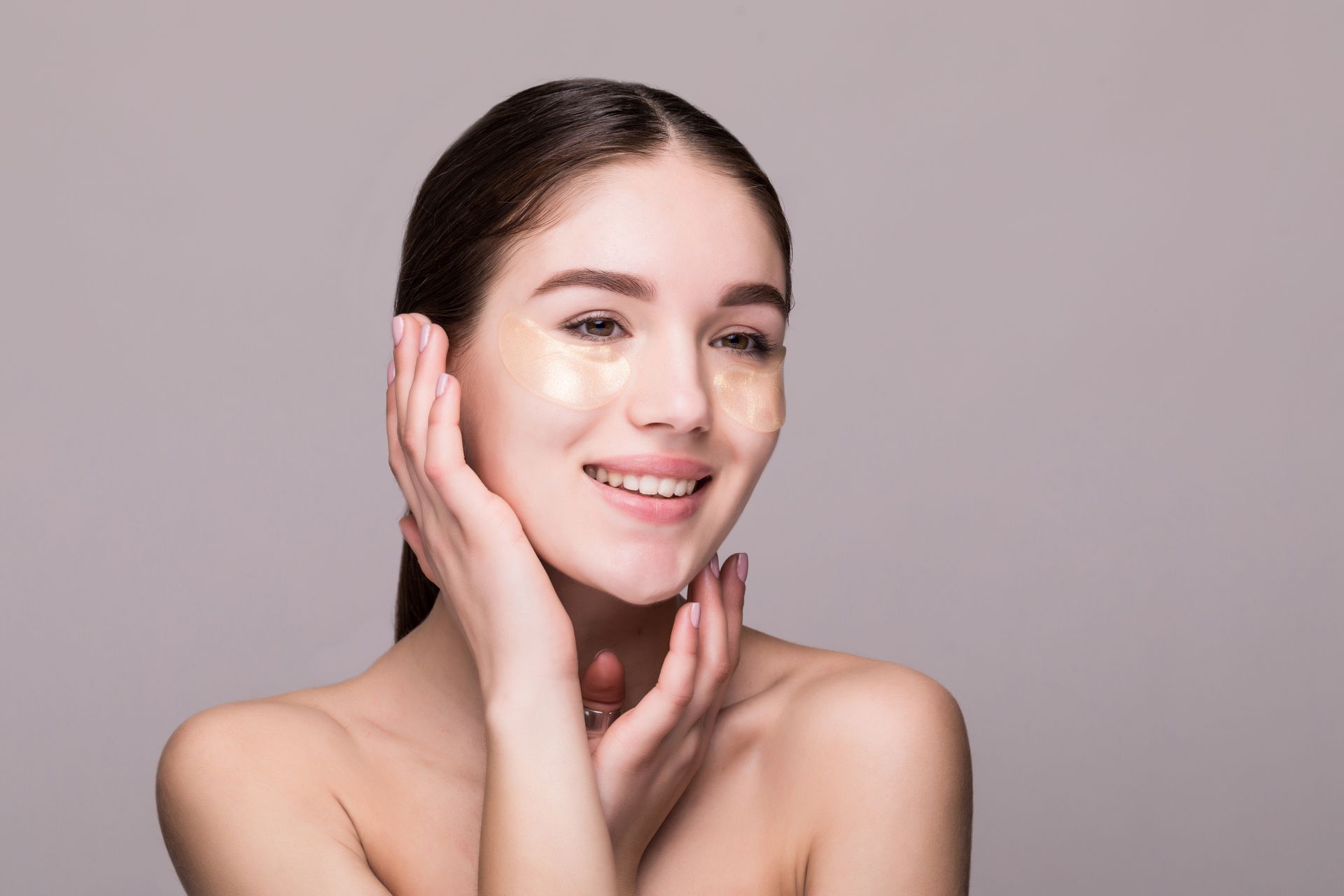 A woman with eye patches on her face is smiling and touching her face.