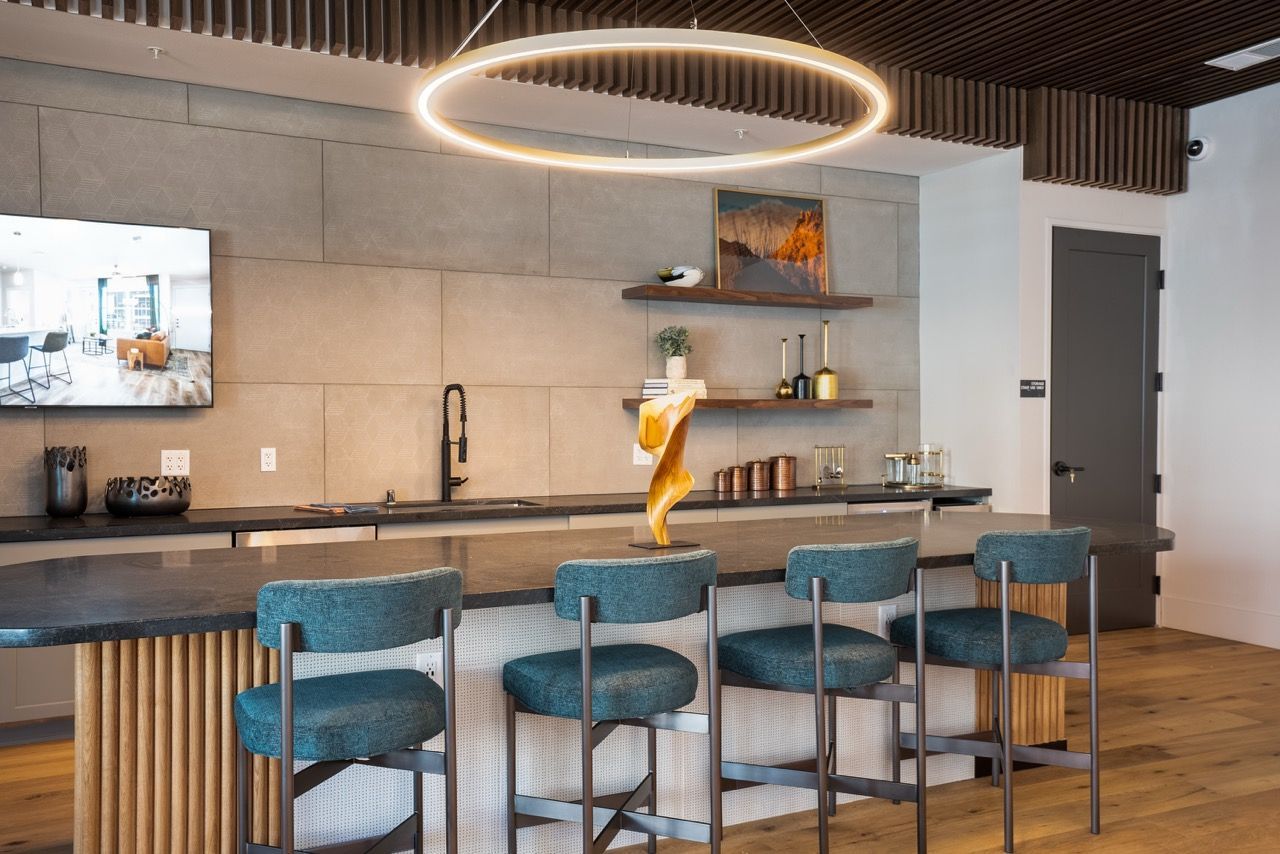 Modern communal kitchen with a long island, teal stools, and a ring-shaped pendant light.