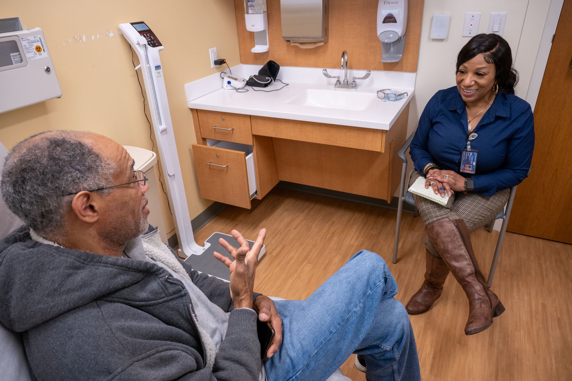 A woman is sitting in a chair talking to a man sitting on a scale