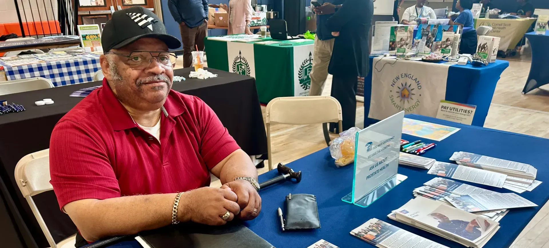 A man in a red shirt is sitting at a table at a convention.