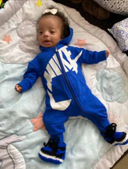 Baby in a blue Nike jumpsuit and crochet booties laying on a patterned blanket.