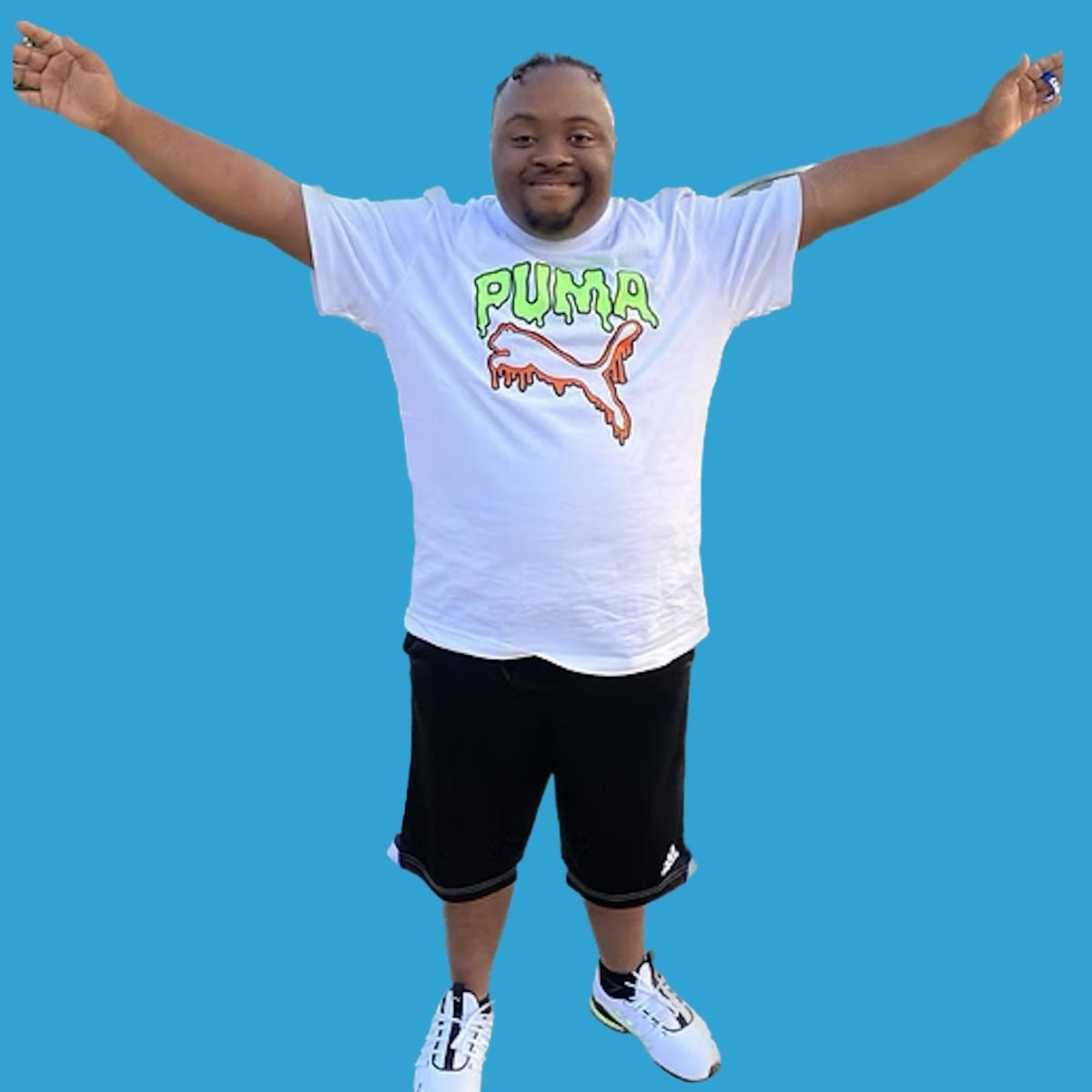 Man with arms outstretched wearing a white Puma shirt, black shorts, and white sneakers, on blue background.