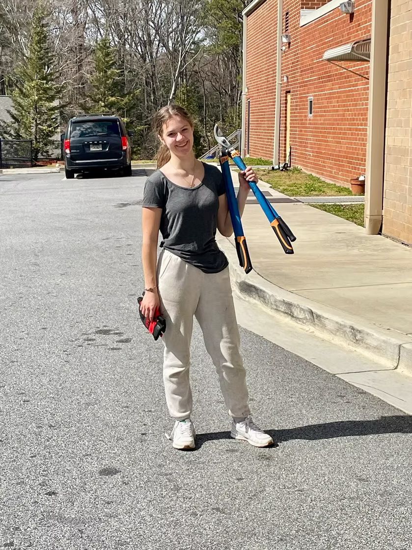 Woman holding tools, standing on a paved area near a building.