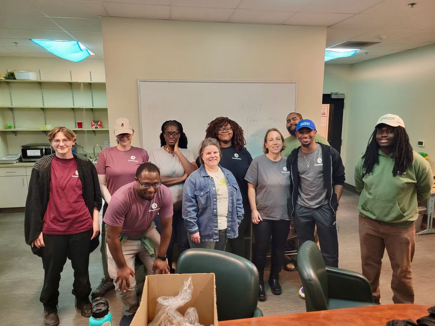Group of people smiling, posing in an office. Some wear matching shirts. A whiteboard is in the background.