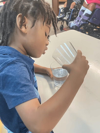 A person in a blue shirt pouring water from a glass into another glass at a table.