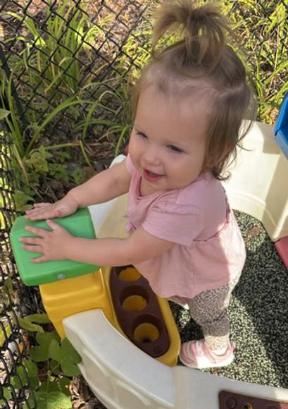 Child playing on colorful toy, smiling with hand on surface.